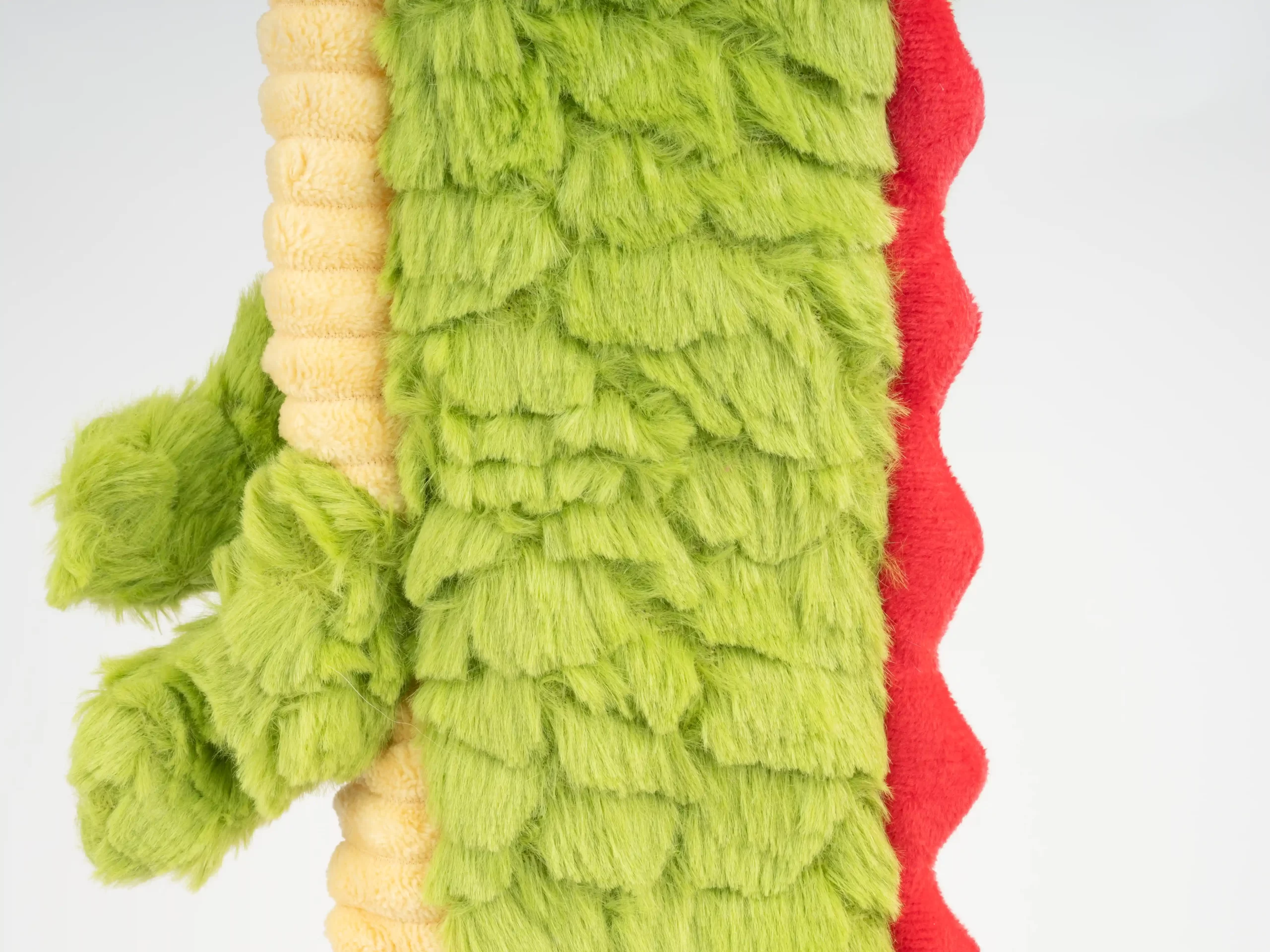 This image highlights the side texture of the green dragon dog toy, featuring overlapping soft scales with bold red accents. The plush material is designed for safe chewing and interactive play, making it a fun and engaging toy for pets.