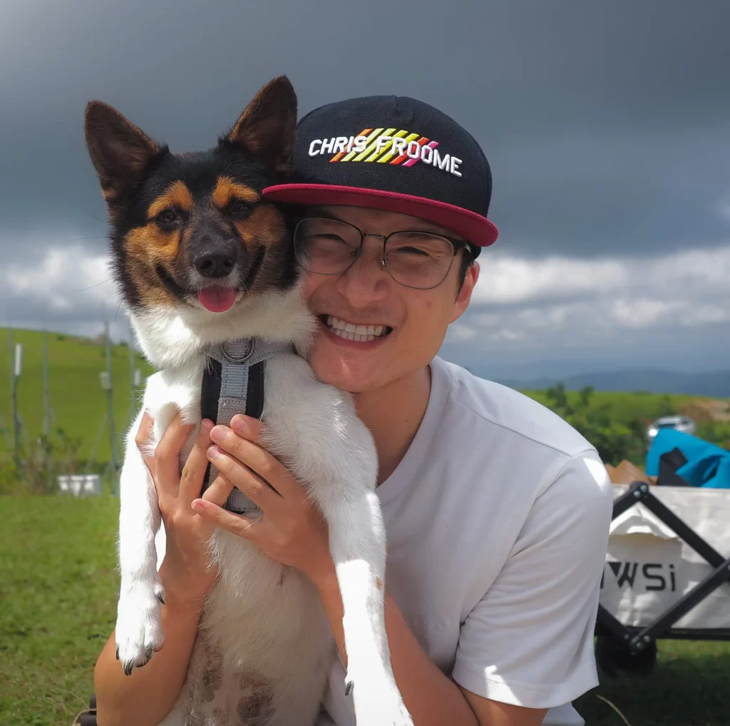 This heartwarming image captures a man holding his happy dog while smiling for the camera. Set against a scenic outdoor backdrop with lush greenery and a cloudy sky, the photo highlights the special bond between pets and their owners. Perfect for use in pet-related promotions or lifestyle content.