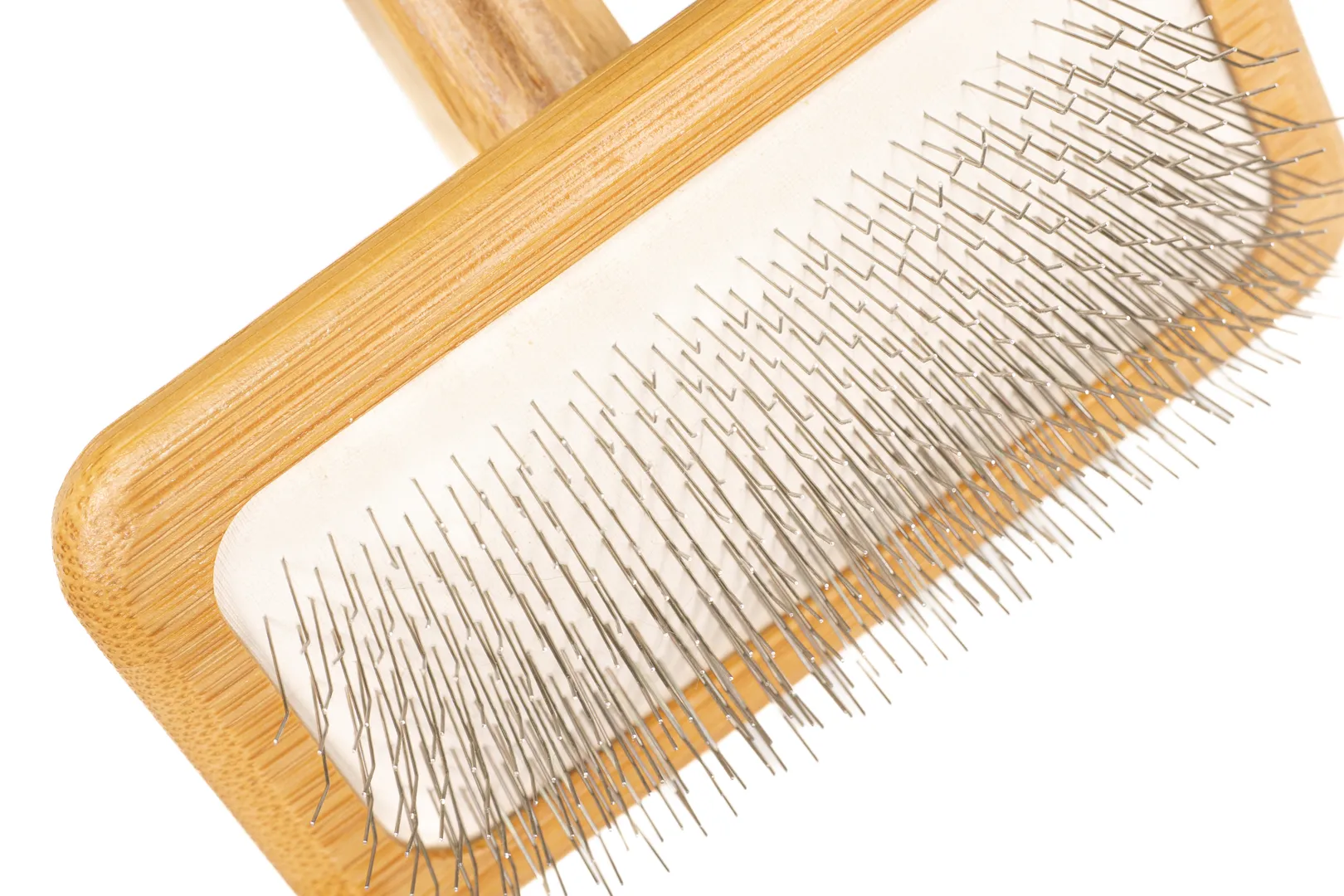 A close-up view of the fine metal pins on the white cushion of a wooden slicker brush for dogs, showing their angled design for grooming.